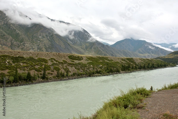 Obraz Thunderclouds low over a picturesque mountain valley with a beautiful river flowing through it on a sunny summer day.