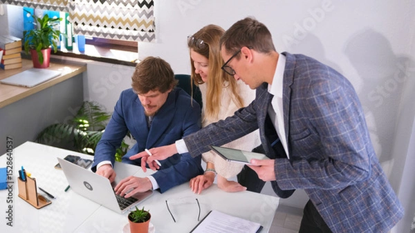 Fototapeta A team of professional marketers is conferring at the head's desk. Two men and a woman are looking at a laptop screen