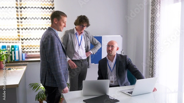 Fototapeta The personable, serious head of the company asks his subordinates for a progress report. Three men in business suits are discussing an important project