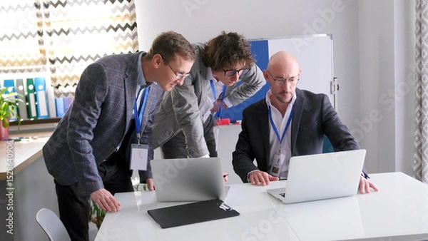 Fototapeta The three co-founders of the business company are carefully looking at the sales statistics on their laptop screen. A group of successful men discuss work