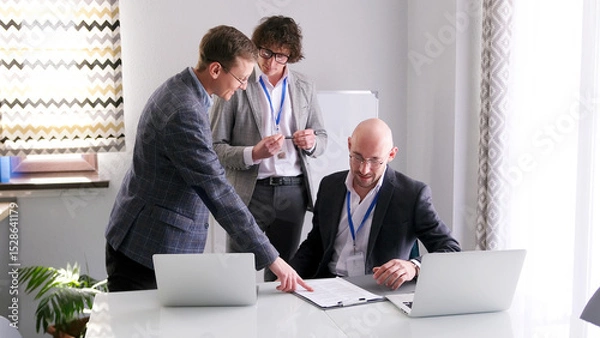 Fototapeta A group of men discusses the details of the contract. One of the men points to something on the paper in front of him