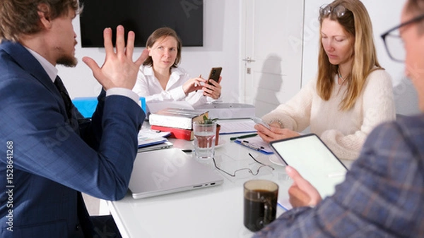 Fototapeta A group of young people are sitting at a table in the conference room of a family office. Teamwork. The scene is intense