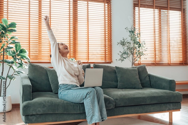 Fototapeta Funny euphoric young asian woman celebrating winning or getting ecommerce shopping offer on computer laptop. Excited happy girl winner looking at notebook celebrating success