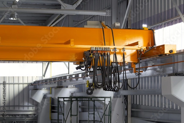 Fototapeta Overhead crane in factory or warehouse. Industrial machine or lifting equipment with hoist, hook and wire rope on beam girder structure for manufacturing production and freight shipping transport.