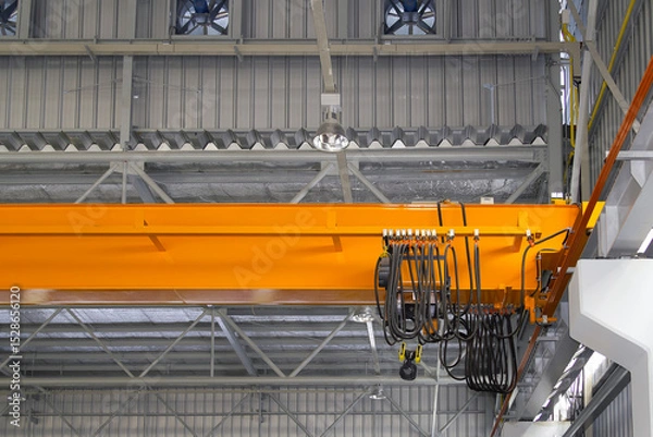 Fototapeta Overhead crane in factory or warehouse. Industrial machine or lifting equipment with hoist, hook and wire rope on beam girder structure for manufacturing production and freight shipping transport.