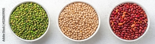 Obraz Three bowls filled with green mung beans, beige soybeans, and red kidney beans arranged side by side on a light surface.