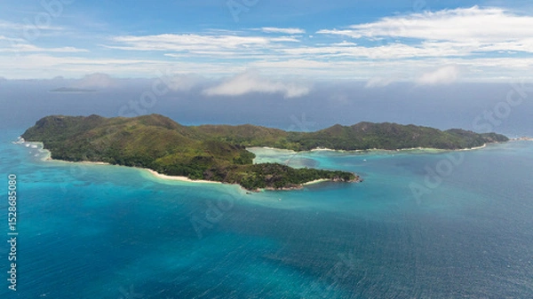 Fototapeta A scenic aerial view of a tropical island with turquoise waters surrounding white sandy beaches and lush greenery. Curieuse, Seychelles.
