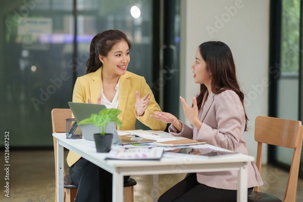Fototapeta Two Asian businesswomen are sitting in a meeting, planning investment plans, business strategies. On the table are documents and graphs.