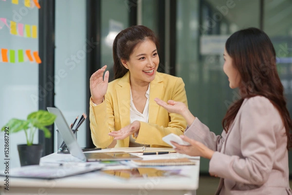 Fototapeta Two Asian businesswomen are sitting in a meeting, planning investment plans, business strategies. On the table are documents and graphs.