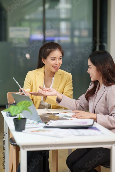 Fototapeta Two Asian businesswomen are sitting in a meeting, planning investment plans, business strategies. On the table are documents and graphs.