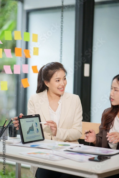 Fototapeta Two Asian businesswomen are sitting in a meeting, planning investment plans, business strategies. On the table are documents and graphs.