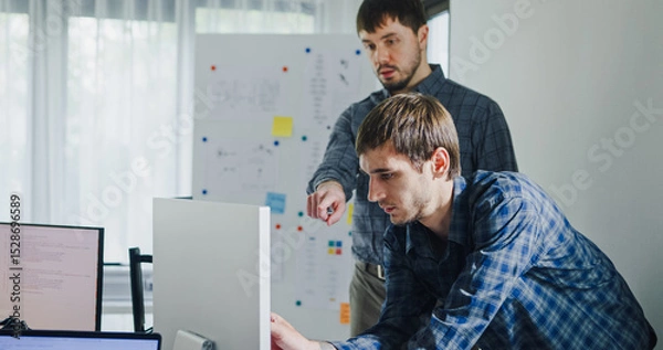 Fototapeta Team adult male engineer collaborate on robotic hand project using AI code solutions machine learning at tech workspace. Artificial intelligence interface, collaboration support prototype development.