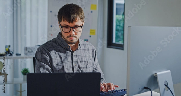 Obraz Young adult male freelance developer typing write prompt AI bot app program nomad terminal with coding at office. Artificial intelligence dashboard, robotics, user interface, machine learning concept.