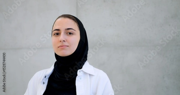 Obraz Professional businesswoman wearing hijab, standing confidently near concrete wall, expressing range of emotions while looking directly toward camera