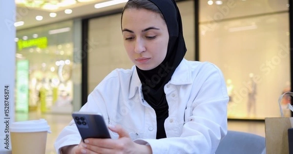 Obraz Young woman engaging with smartphone while enjoying coffee in trendy cafe, embodying modern digital connectivity and leisurely urban lifestyle during focused moment of communication