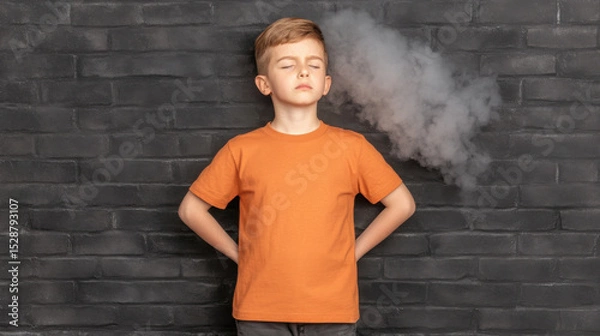 Obraz Boy with orange shirt standing confidently in front of dark brick wall with smoke effect behind him, expression of inspiration