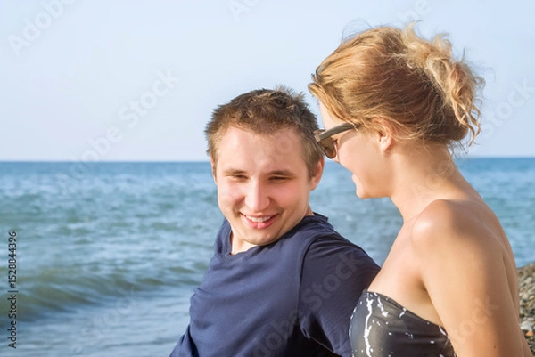 Fototapeta A young guy and a girl are talking on the beach against the background of the blue sea and blue sky on a sunny summer day