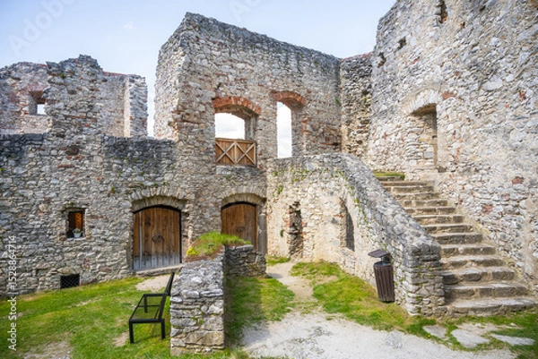 Fototapeta Visitors wander through the historic courtyard of Rabi Castle in Czechia, admiring the ancient stone walls and remnants of architecture under a clear blue sky.
