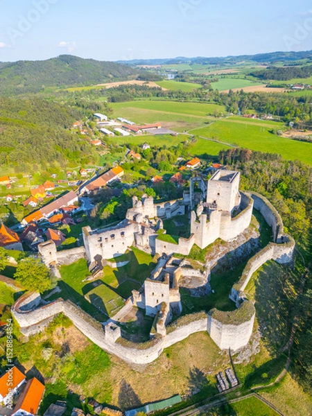 Fototapeta Aerial view showcases the historic Rabi Castle ruins surrounded by lush green fields and small village homes in Czechia. The structure reflects medieval architecture and rich history.