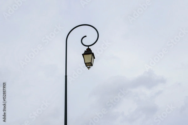 Fototapeta Vintage lamp post stands elegantly against a cloudy sky in a charming urban setting