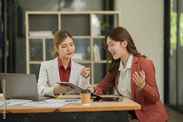 Fototapeta Two Asian businesswomen using laptops, on the table there are graph documents working on business investment.