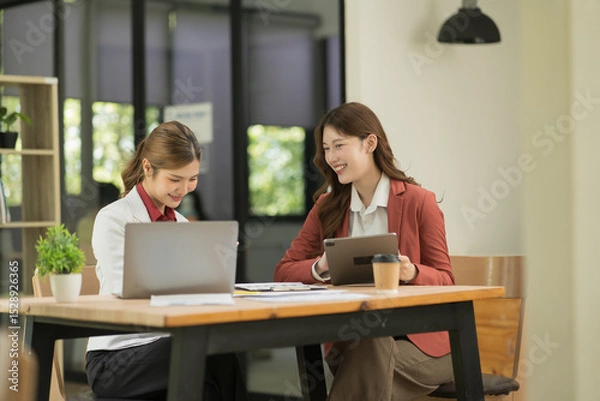 Fototapeta Two Asian businesswomen using laptops, on the table there are graph documents working on business investment.