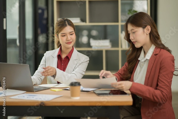 Fototapeta Asian businesswoman sitting in a meeting, talking about a document and chart placed on the table.