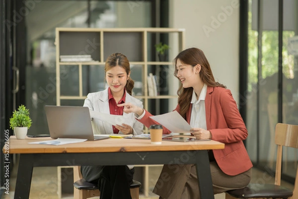 Fototapeta Two Asian businesswomen using laptops, on the table there are graph documents working on business investment.