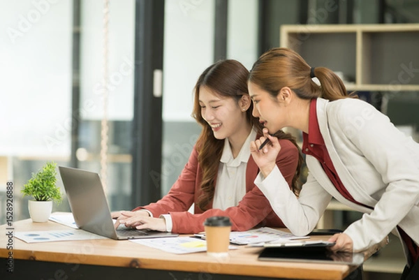 Fototapeta Two Asian businesswomen using laptops, on the table there are graph documents working on business investment.