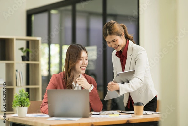 Fototapeta Two Asian businesswomen using laptops, on the table there are graph documents working on business investment.