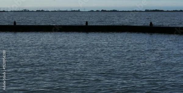 Fototapeta Narrow port wall at dusk in Oudega Friesland Netherlands, on the horizon many wind energy turbines. A politically controversial topic