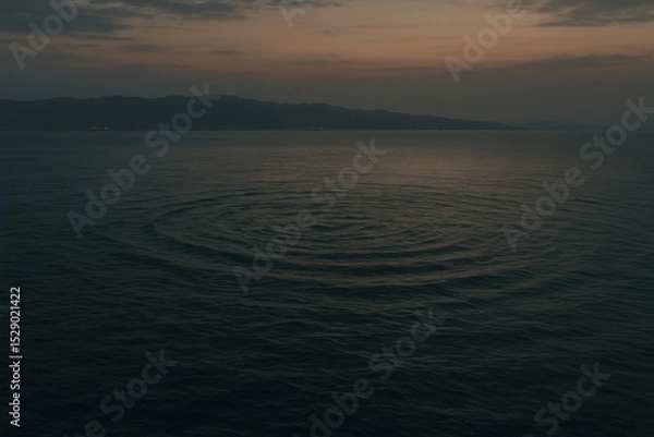 Obraz Gentle ripples spread across a calm lake at dusk, with mountains silhouetted in the distance under a twilight sky.