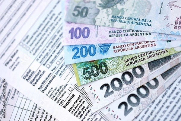 Fototapeta Argentine pesos money bills in big amount lies on table with pen and tax forms close up