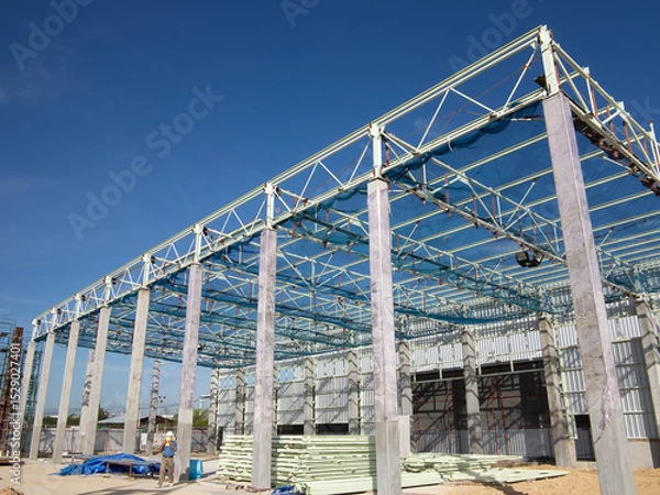 Fototapeta Roof under construction in construction site . To election or assembly frame truss, steel structure for cover factory warehouse building. Include scaffolding and safety net to prevent worker falling.