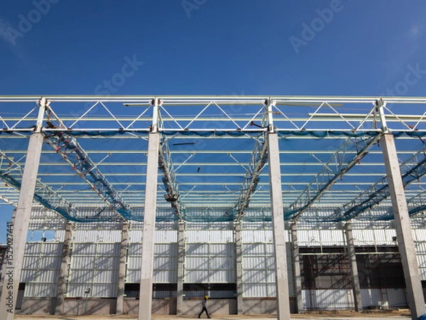 Fototapeta Roof under construction in construction site . To election or assembly frame truss, steel structure for cover factory warehouse building. Include scaffolding and safety net to prevent worker falling.