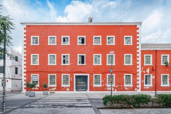 Fototapeta Striking Red Building With White Trim And Multiple Windows In A Menorcan Town. Mediterranean Architecture, Vibrant Facade, Spanish Island Life, Urban Scene
