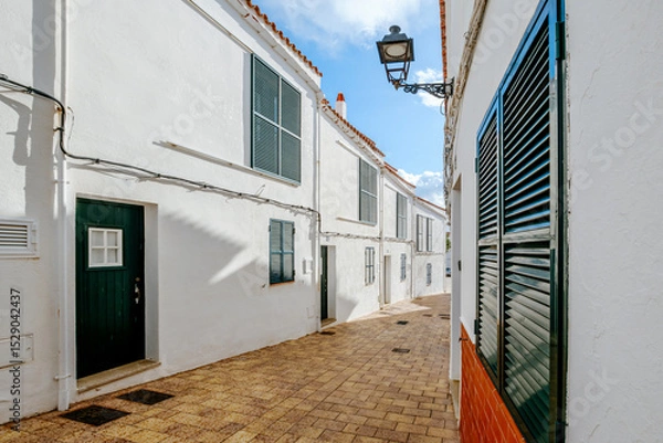Fototapeta Quaint Whitewashed Street With Green Shutters In A Traditional Menorcan Village. Balearic Islands Architecture, Sunny Day, Spanish Island Charm