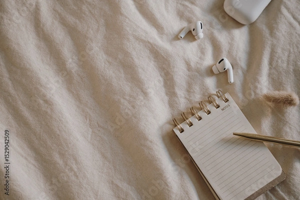 Fototapeta Flat Lay of Notebook and Earbuds on Soft Fabric