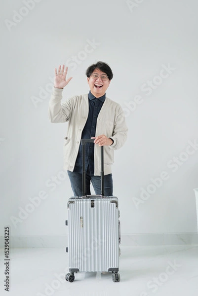 Fototapeta A man is standing next to a suitcase and waving