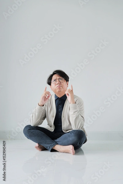 Fototapeta A man is sitting on the floor with his hands in the air