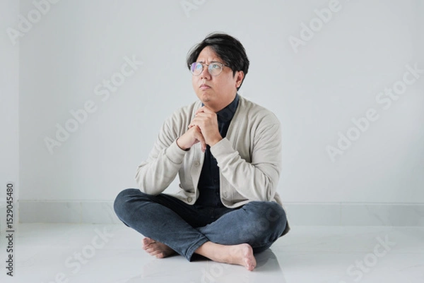Fototapeta A man is sitting on the floor with his hands clasped in front of him