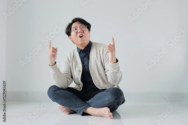 Fototapeta A man is sitting on the floor with his hands up in the air