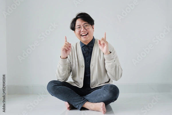 Fototapeta A man is sitting on the floor with his arms raised and pointing to the sky