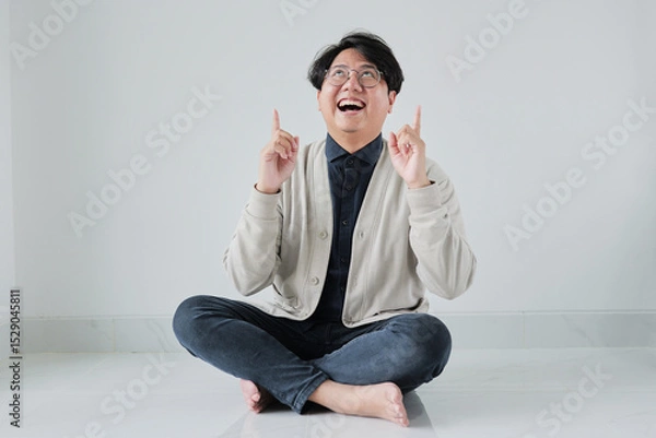 Fototapeta A man is sitting on the floor with his hands up in the air