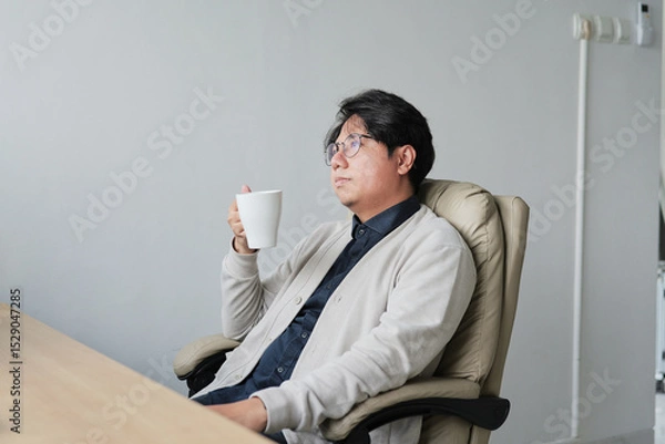Fototapeta A man is sitting in a chair with a white cup in his hand