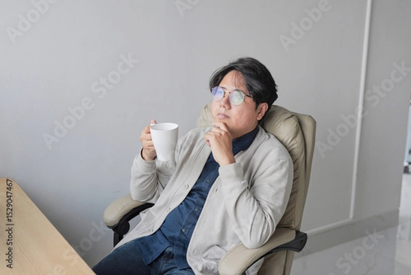 Fototapeta A man is sitting in a chair with a cup in his hand