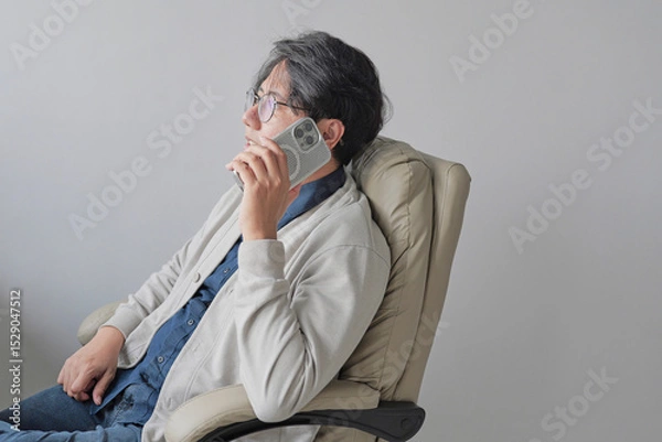 Fototapeta A man is sitting in a chair and talking on his cell phone