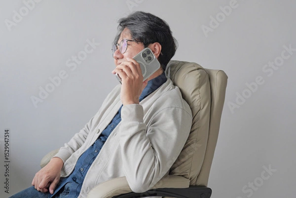 Fototapeta A man is sitting in a chair and talking on his cell phone