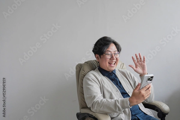 Fototapeta A man is sitting in a chair and holding a cell phone