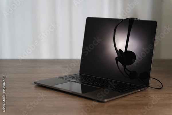 Obraz All center and customer service sleek laptop with black headset resting its screen, placed wooden table minimalistic setting, creating